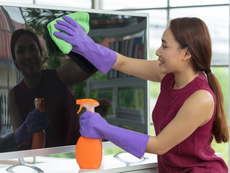 Kobieta myje ekran telewizora. Obrazek w artykule Czym wyczyścić ekran telewizora? Wszystko o delikatnych sposobach czyszczenia ekranów i monitorów