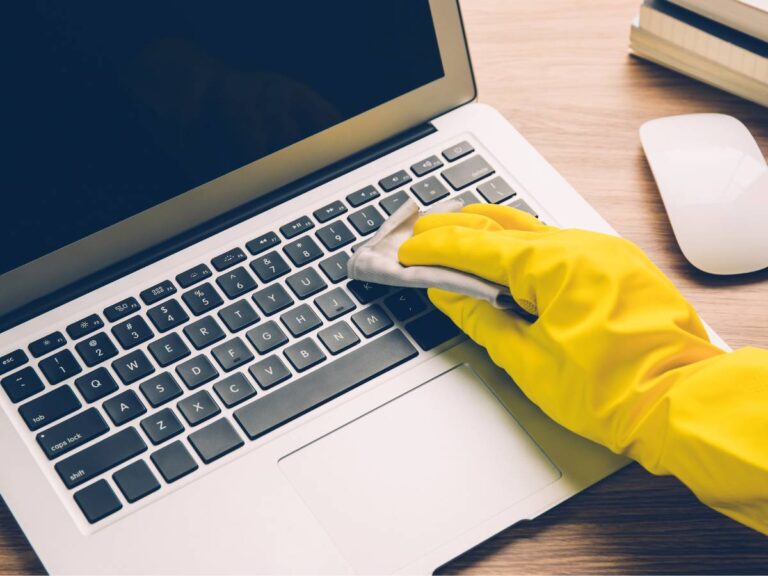 Ręka w żółtej rękawicy czyści klawiaturę laptopa. Obrazek w artykule Jak wyczyścić klawiaturę, aby wyglądała jak nowa? Praktyczne porady
