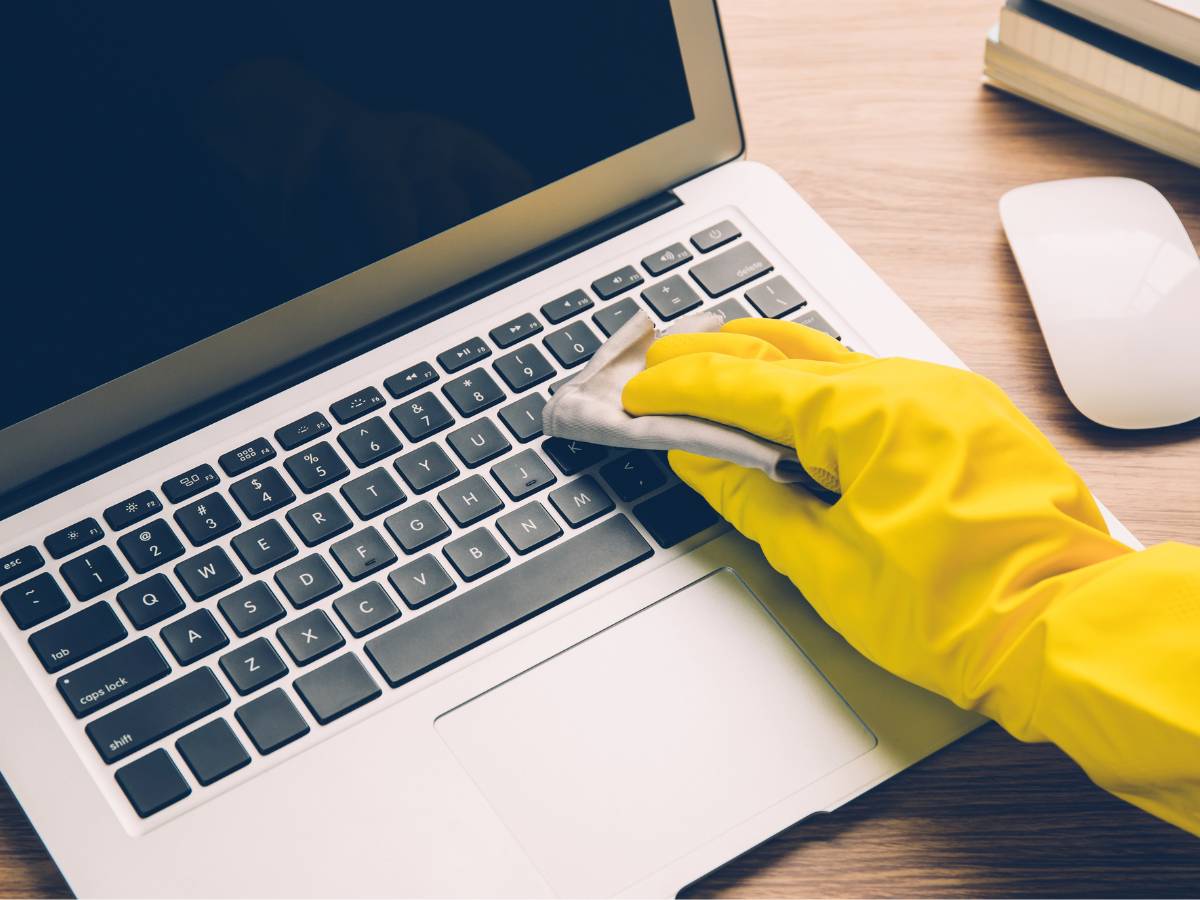 Ręka w żółtej rękawicy czyści klawiaturę laptopa. Obrazek w artykule Jak wyczyścić klawiaturę, aby wyglądała jak nowa? Praktyczne porady